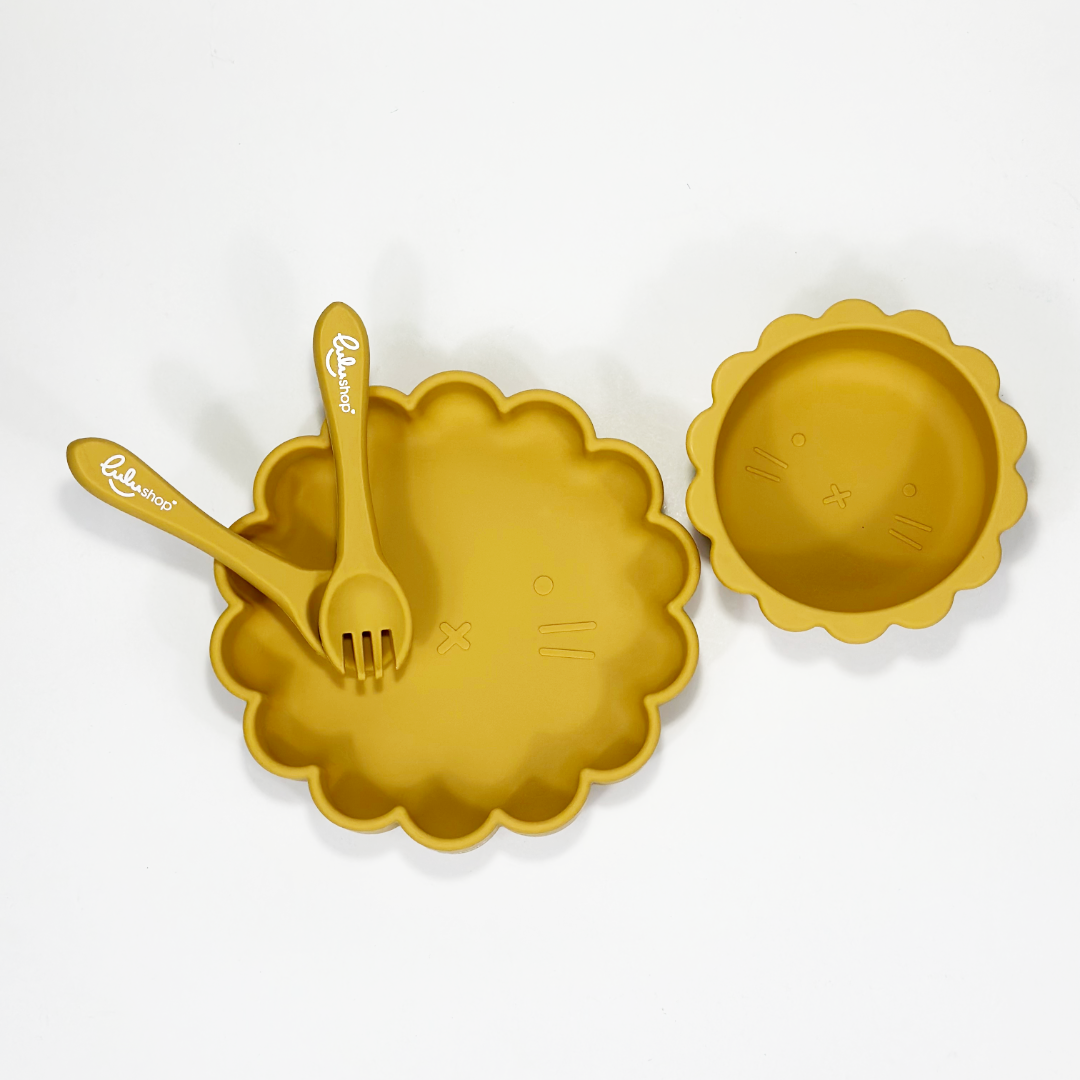 Yellow sunshine-shaped silicone baby feeding set photographed from top view, showing plate, bowl, fork and spoon